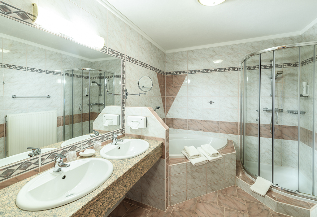 Helles Badezimmer mit zwei Waschbecken, Spiegel und Handtüchern, Badewanne, Dusche