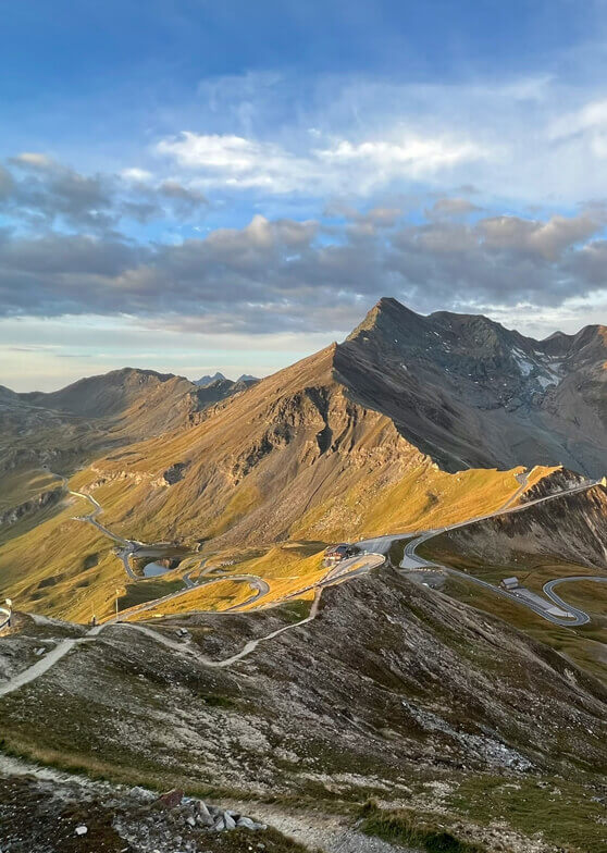 Berge und kurvige Passstraße im goldenen Abendlicht.