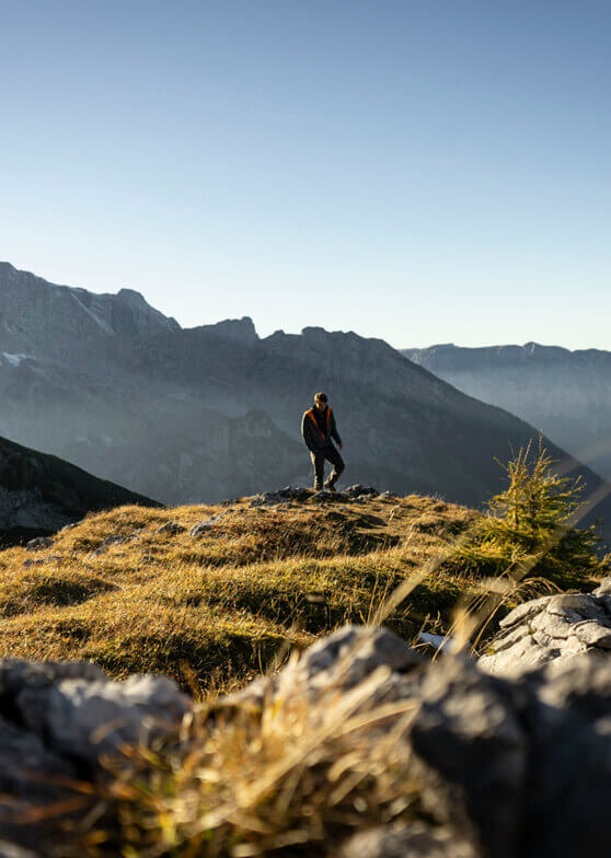 Person auf felsiger Anhöhe vor dunstigen Bergen.