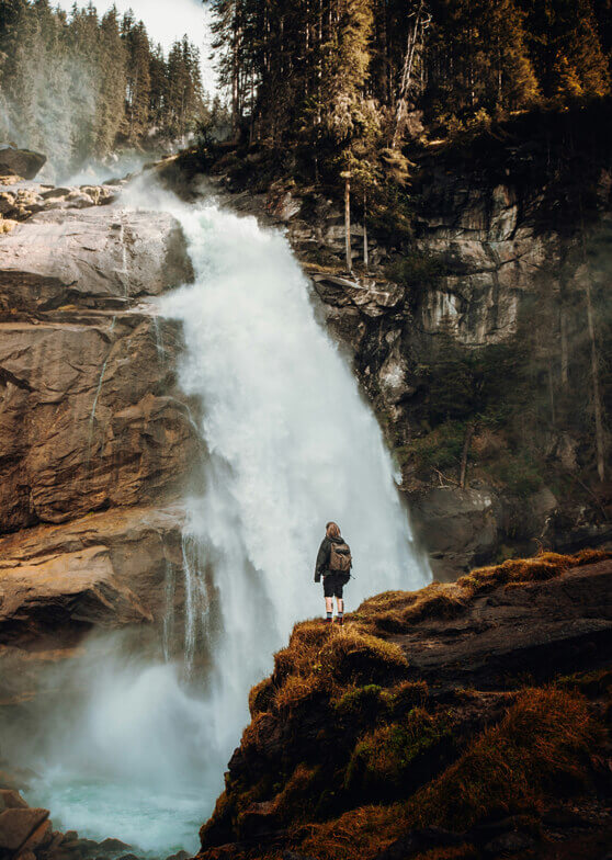 Person mit Rucksack vor mächtigem Wasserfall.