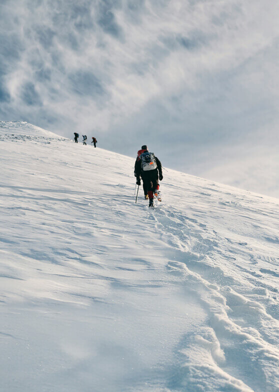 Mehrere Wanderer steigen verschneiten Hang hinauf.
