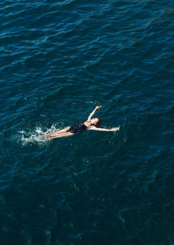 Person in Badeanzug treibt auf dem Rücken im blauen Wasser.