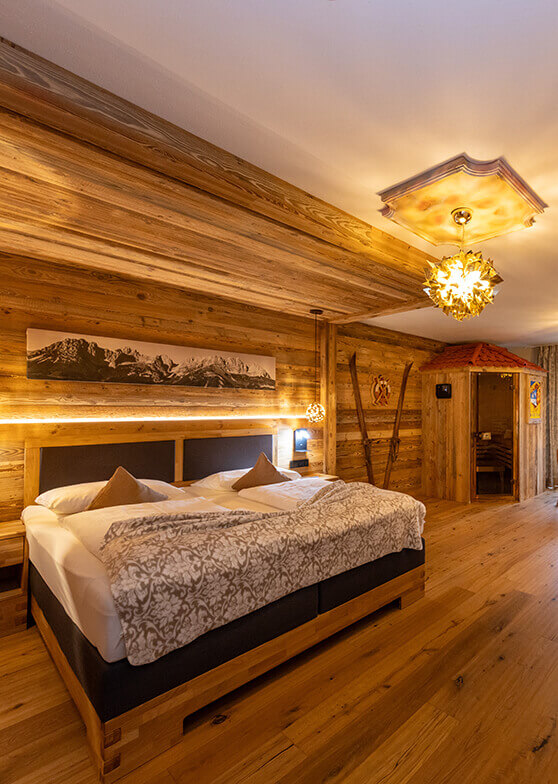 Holzhotelzimmer mit Bett, Sauna, Skiern, Bergbild.
