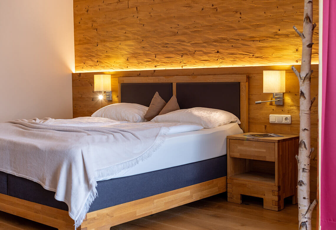 Schlafzimmer mit Doppelbett, Holzwand, Nachttisch.