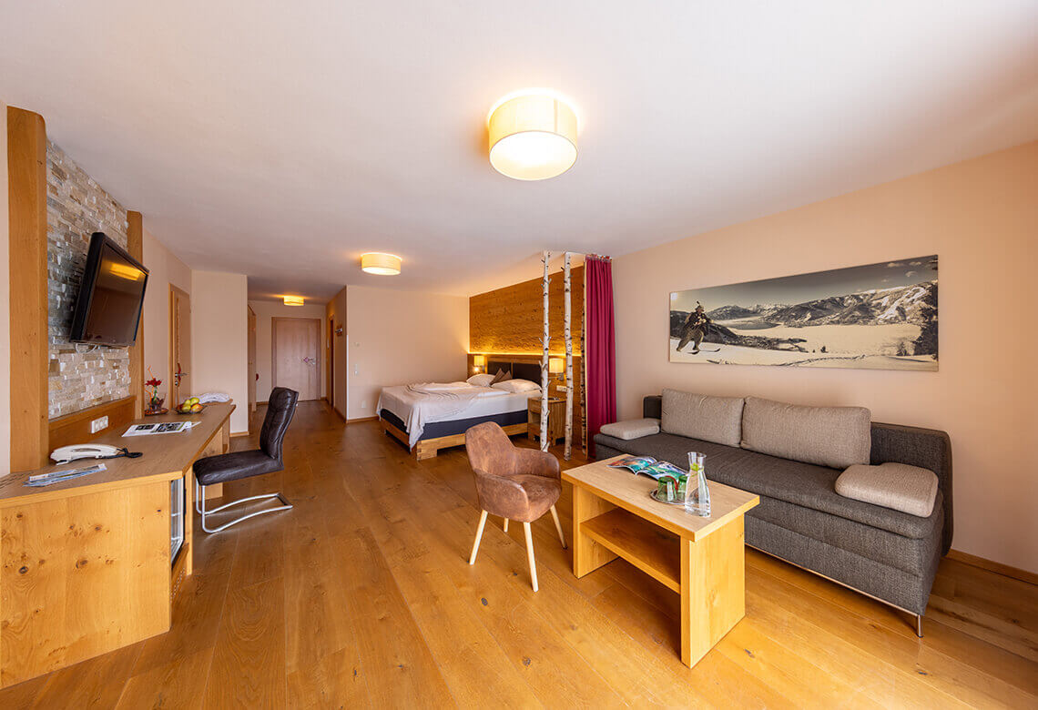 Helles Hotelzimmer mit Doppelbett, Sofa, Schreibtisch, TV.