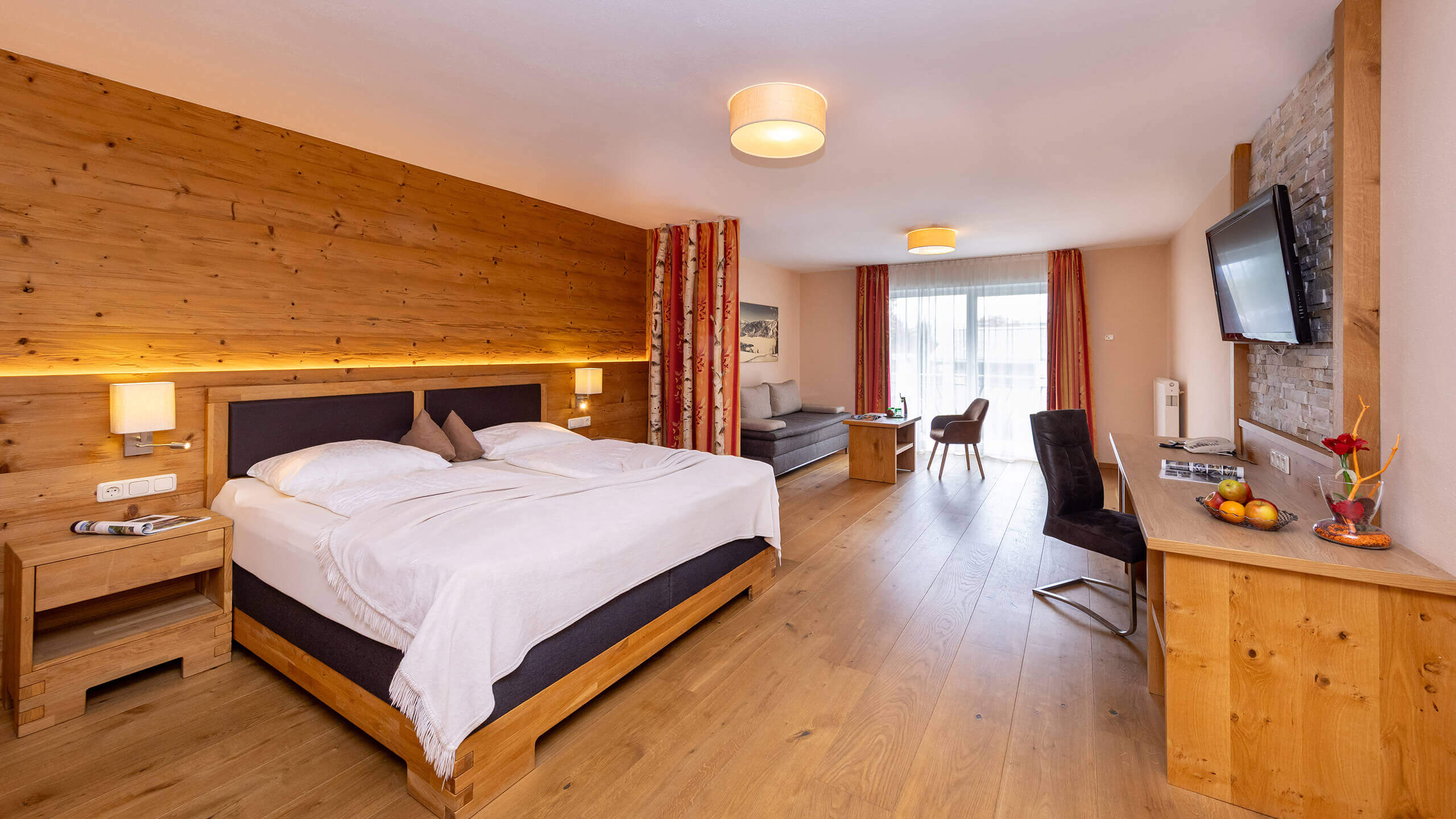 Hotelzimmer mit Holzwänden, großem Bett, Sofa und Schreibtisch.