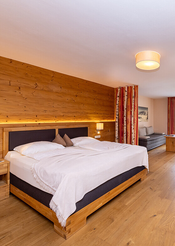 Schlafzimmer mit Holzwand, Doppelbett und Sofa.