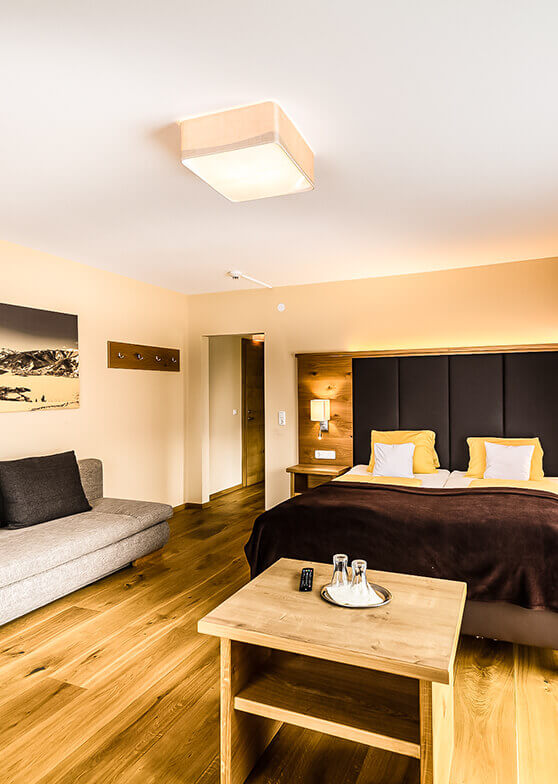 Helles Hotelzimmer mit Doppelbett, Sofa, Holzboden.