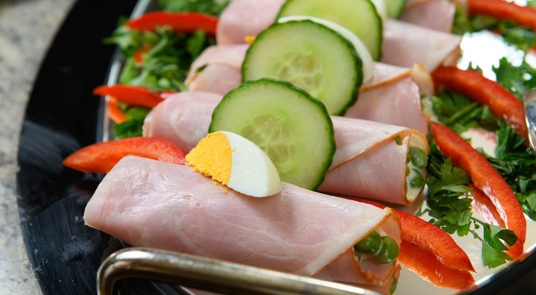 Schinkenröllchen mit Erbsen, Gurke, Ei, Paprika auf Teller.