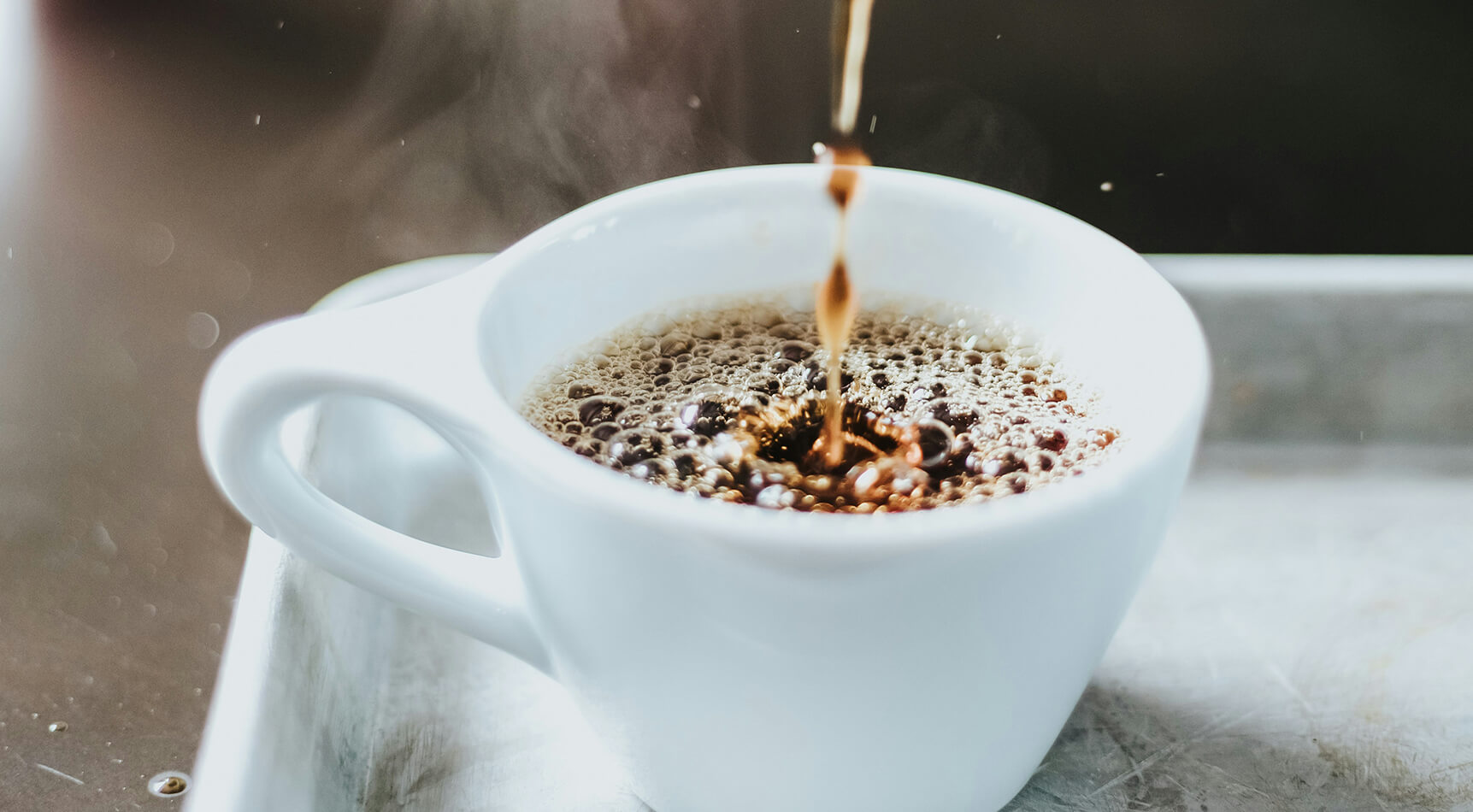 Kaffee wird in weiße Tasse gegossen mit Dampf und Bläschen.