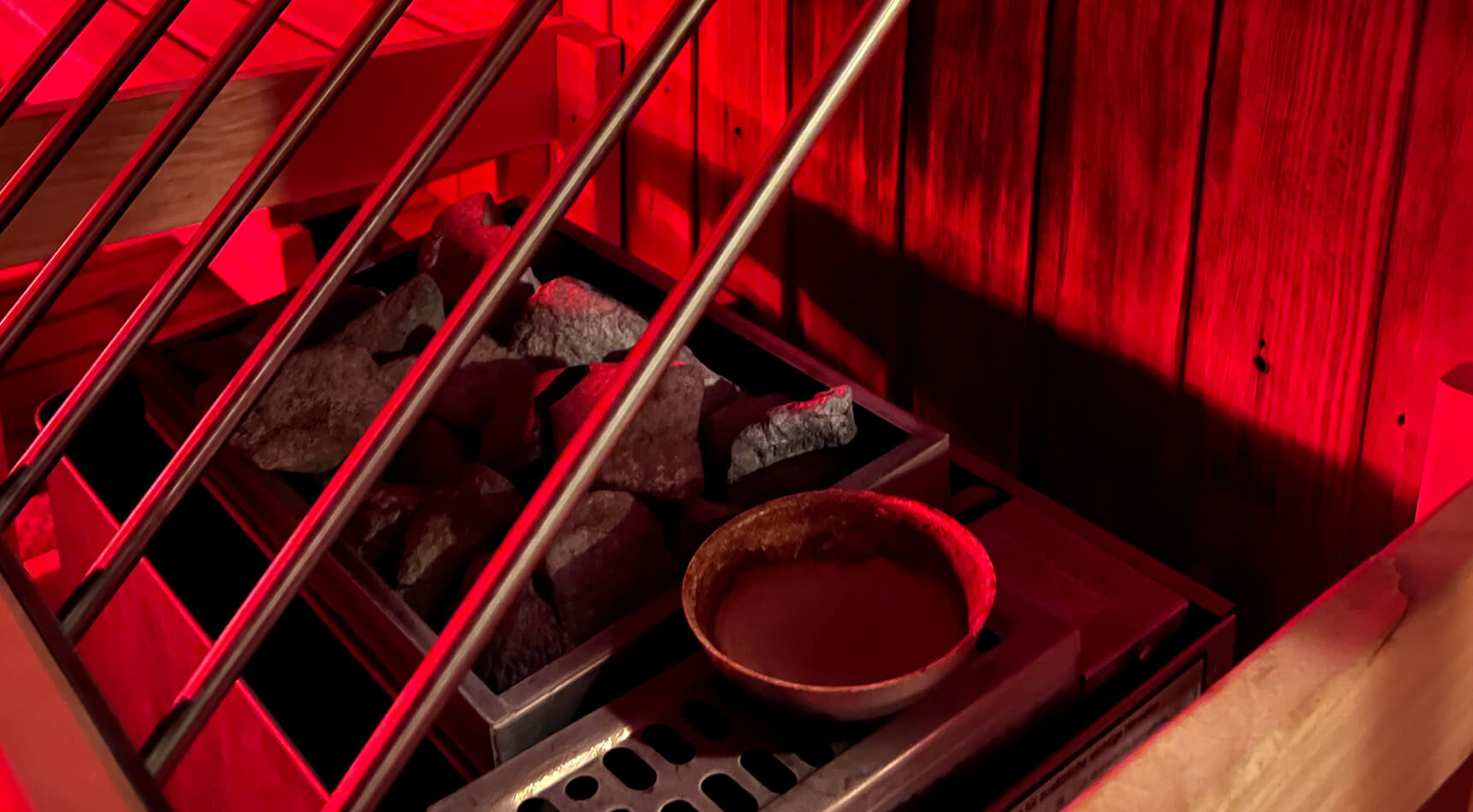 Saunaofen mit Steinen und Schale im Rotlicht.