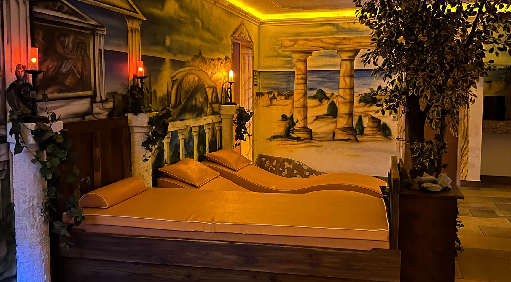 Zwei orange Liegen in einem Raum mit antiker Wandmalerei.