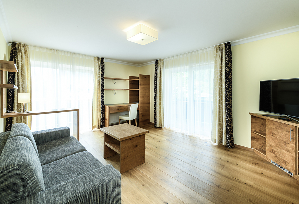 Wohnzimmer mit Sofa, Sessel, Tisch, TV, Fenster