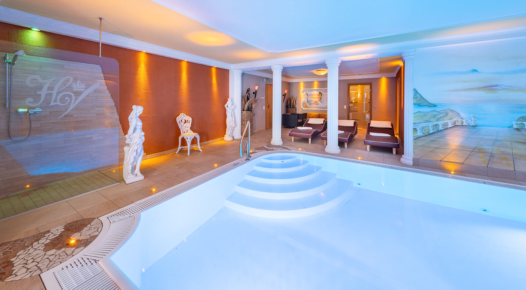 Beleuchteter Innenpool mit Säulen, Wandmalerei und Liegen.