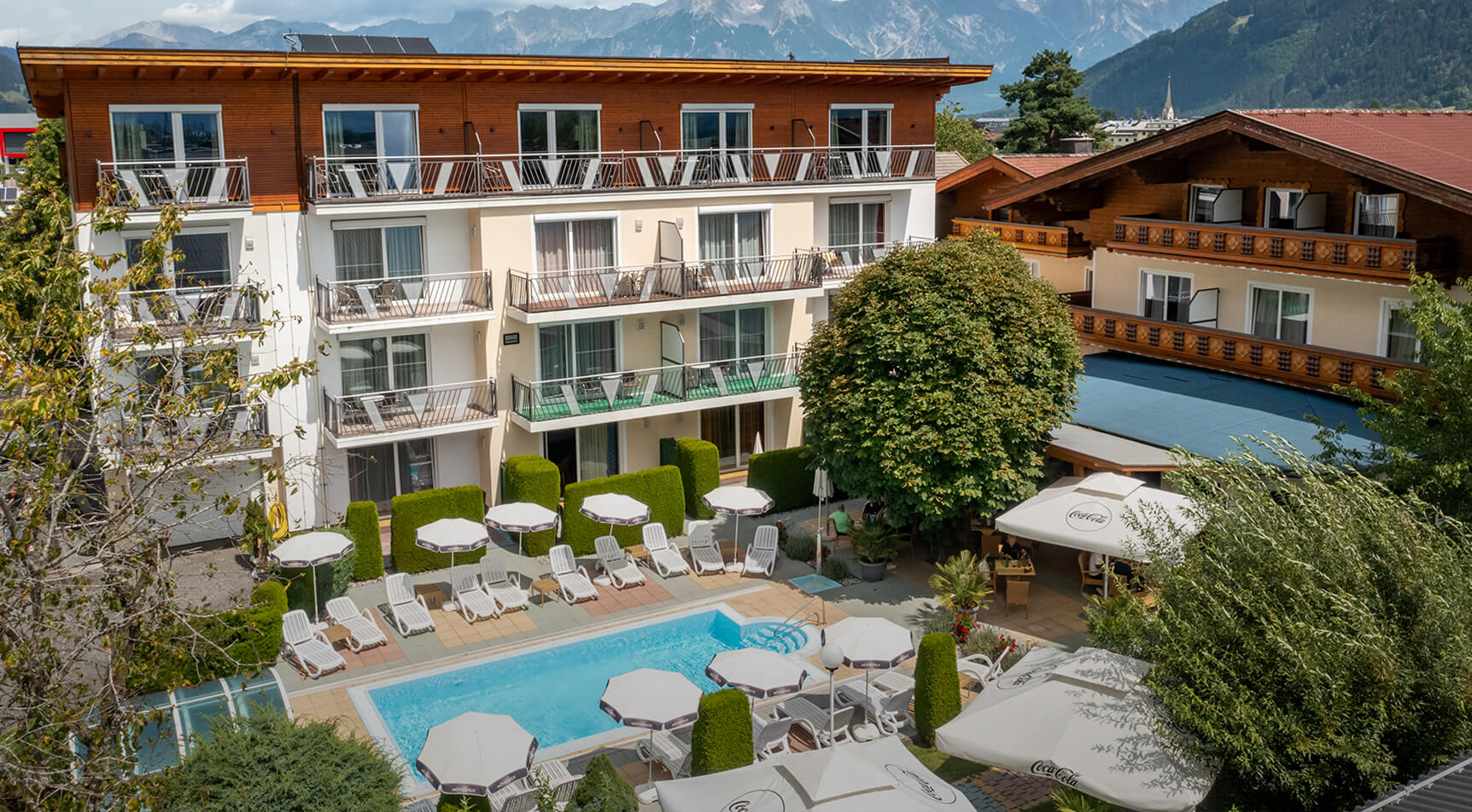 Hotel mit Balkonen, Poolbereich, Liegen und Bergblick.