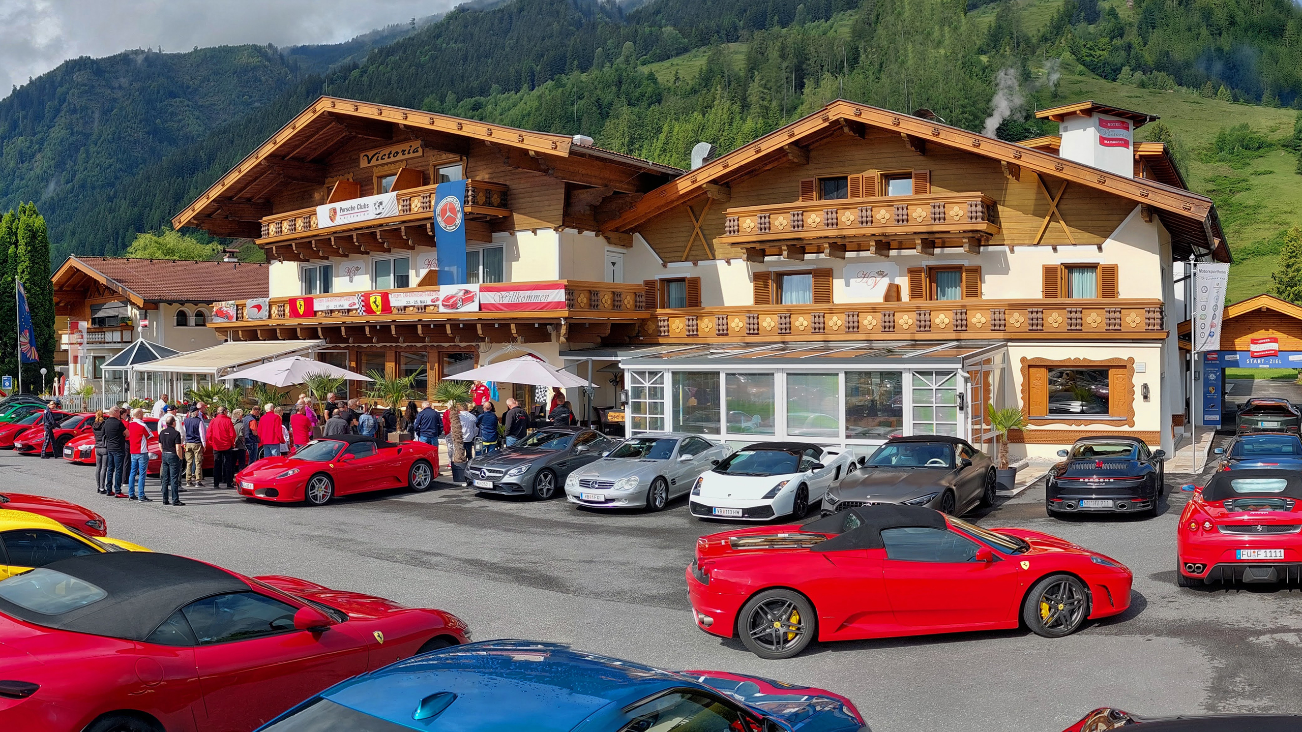 Luxusautos vor Alpenhotel mit Bergen.