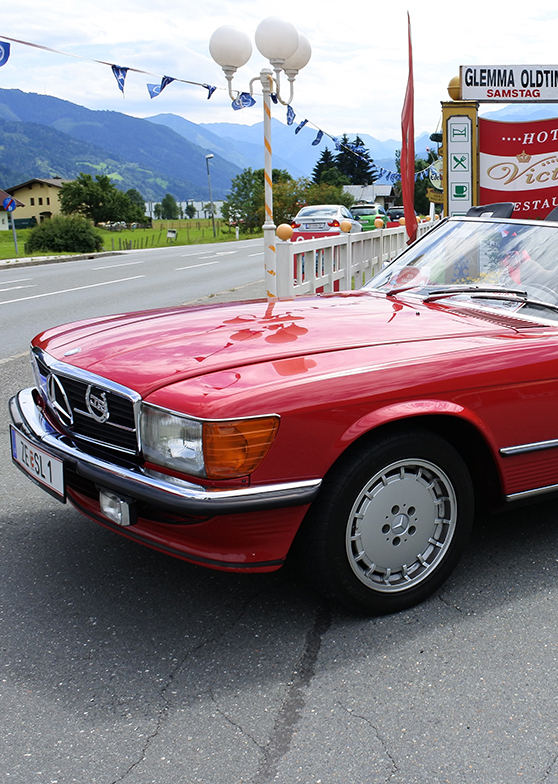 Rotes Oldtimer-Cabrio am Straßenrand, Berge dahinter.