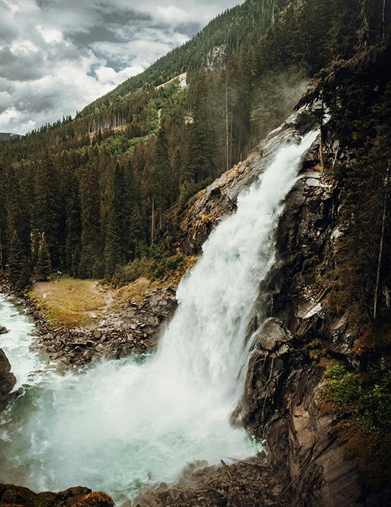 Wasserfall in bewaldeter Berglandschaft mit Fluss.