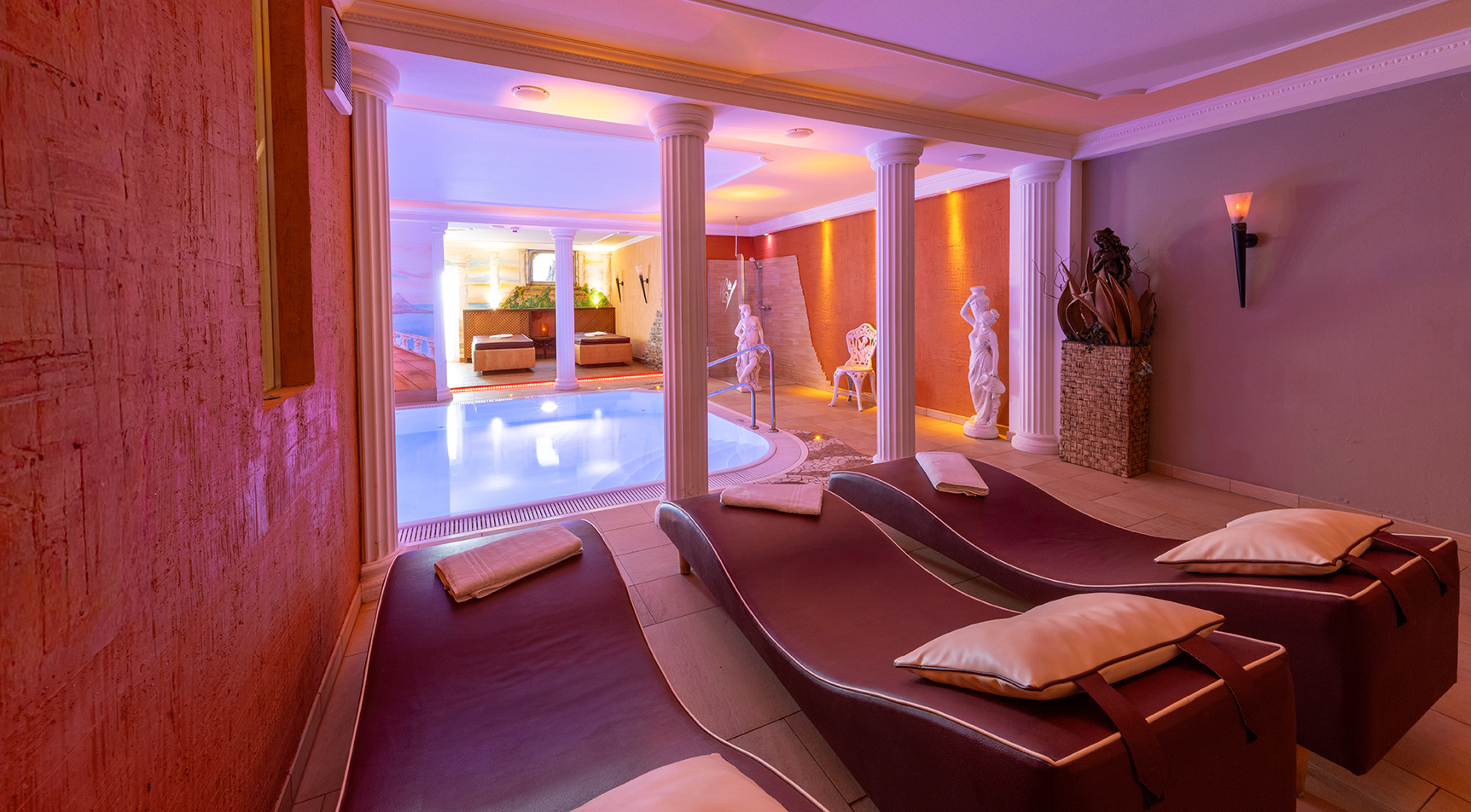 Wellnessbereich mit Pool, Liegen, Säulen und Statuen.