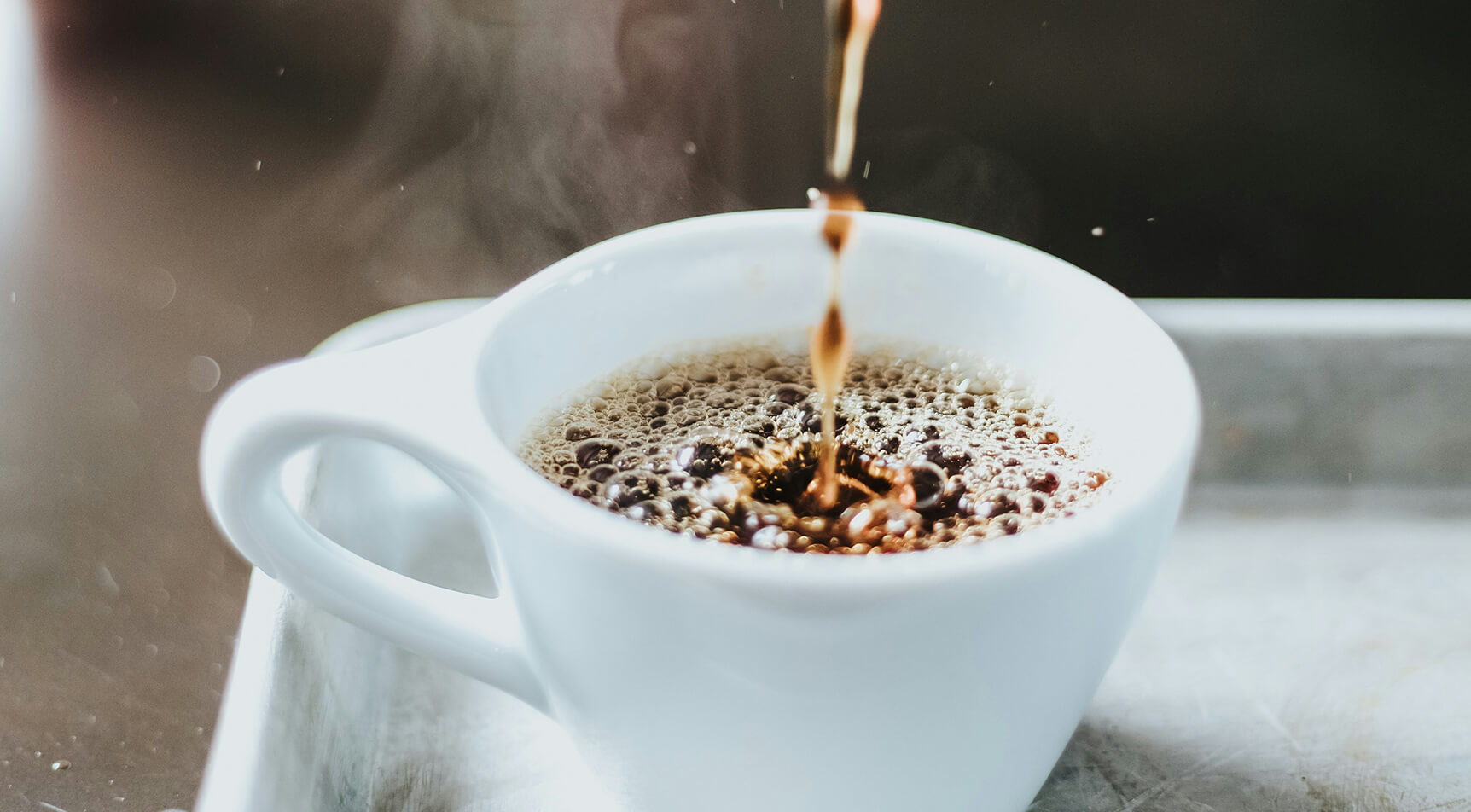 Kaffee gießt in weiße Tasse, Bläschen und Dampf.