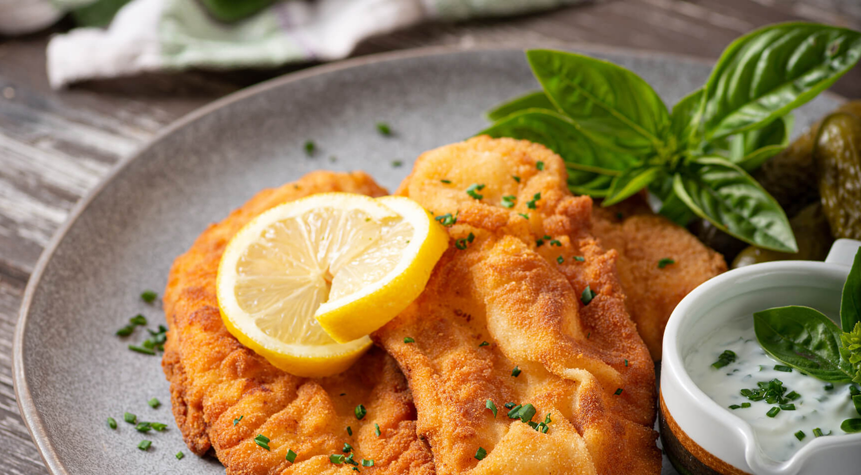 Goldbraune Schnitzel mit Zitrone, Kräuterdip, Gurken.