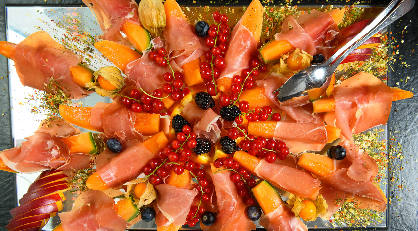 Servierplatte mit Schinken, Melone, Beeren und Physalis.
