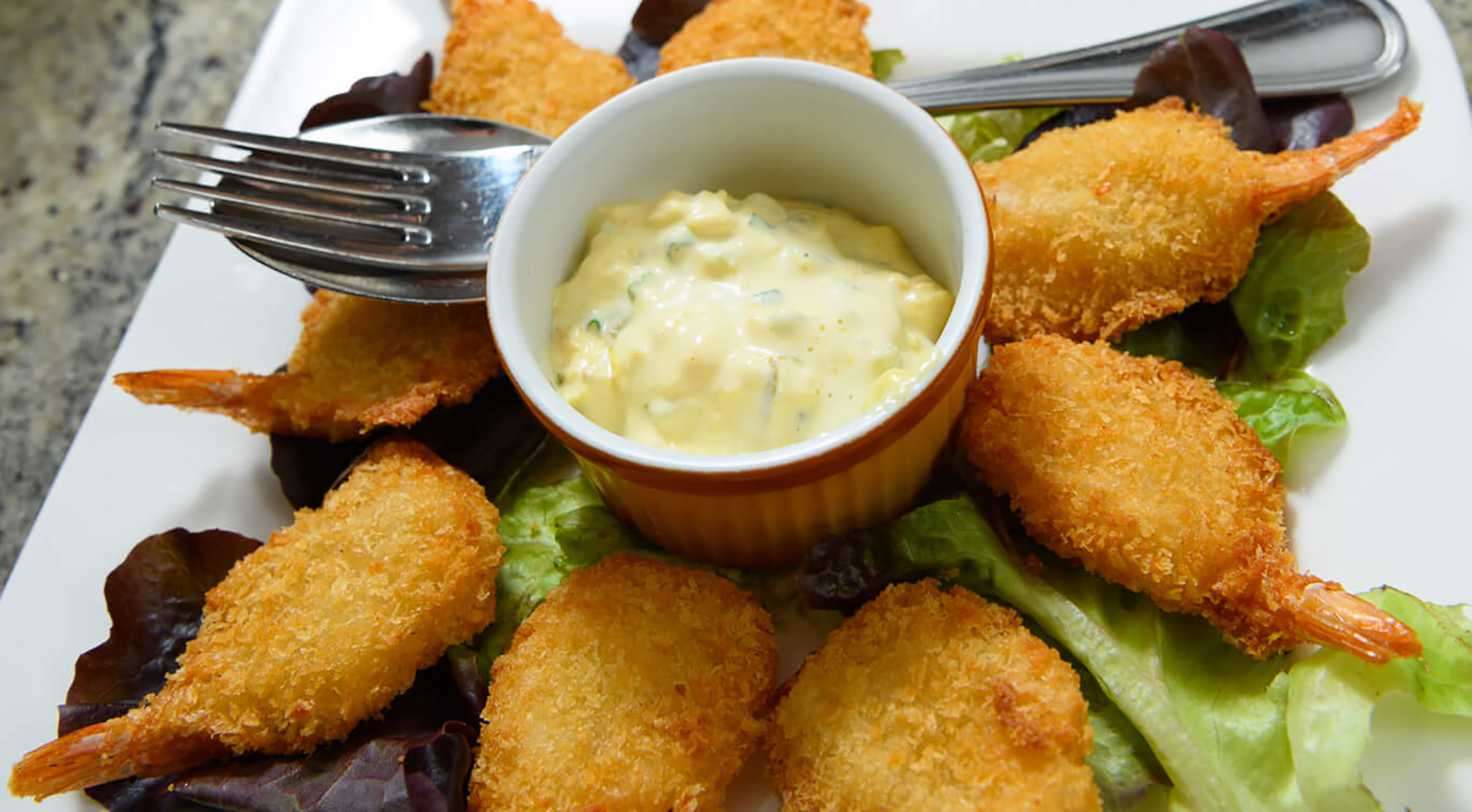 Panierte Garnelen und Dip auf Salat mit Besteck.