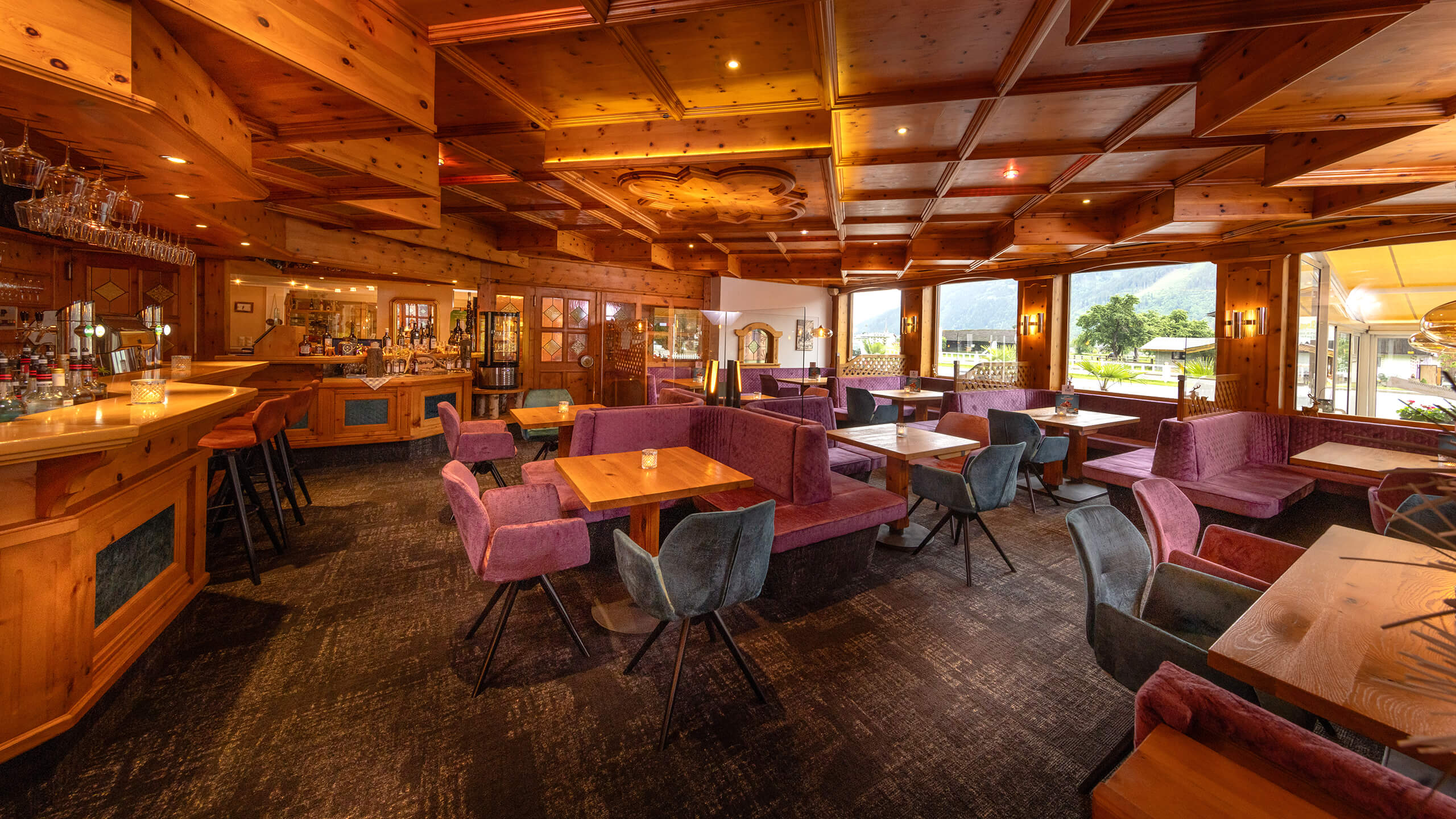 Restaurant mit Holzeinrichtung, Bar, lila Sitzen und Fensterblick.