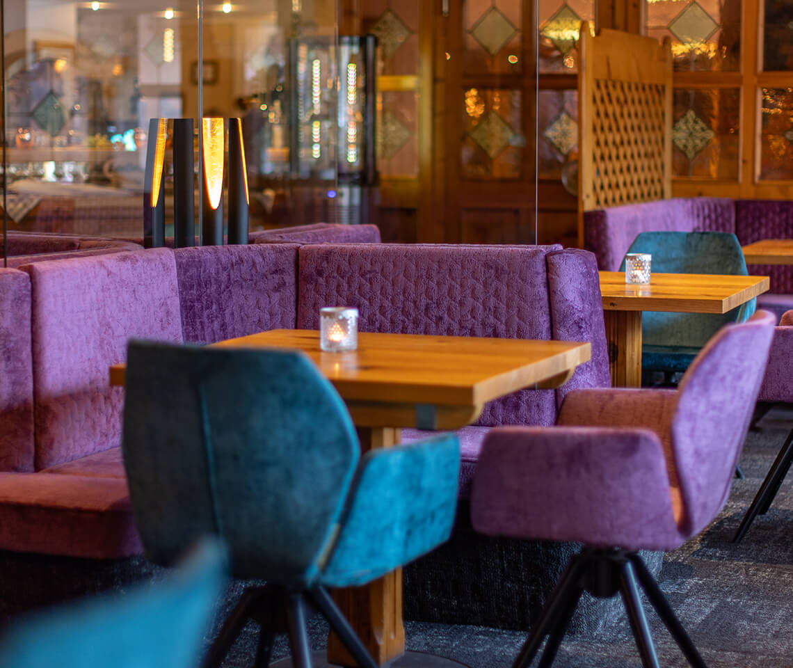 Lila Bänke, Holztische, türkise Stühle mit Kerzen.