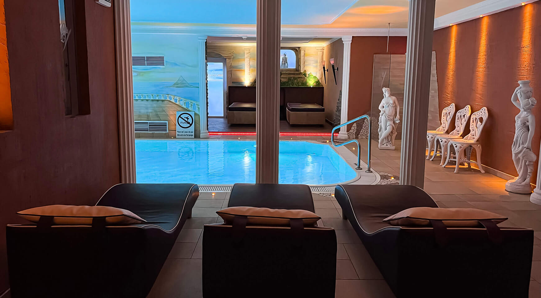 Innenpoolbereich mit Liegen, Säulen und Statuen.