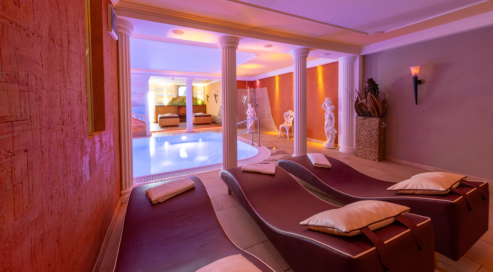 Spa-Bereich mit Pool, Liegen und Säulen, violett beleuchtet.