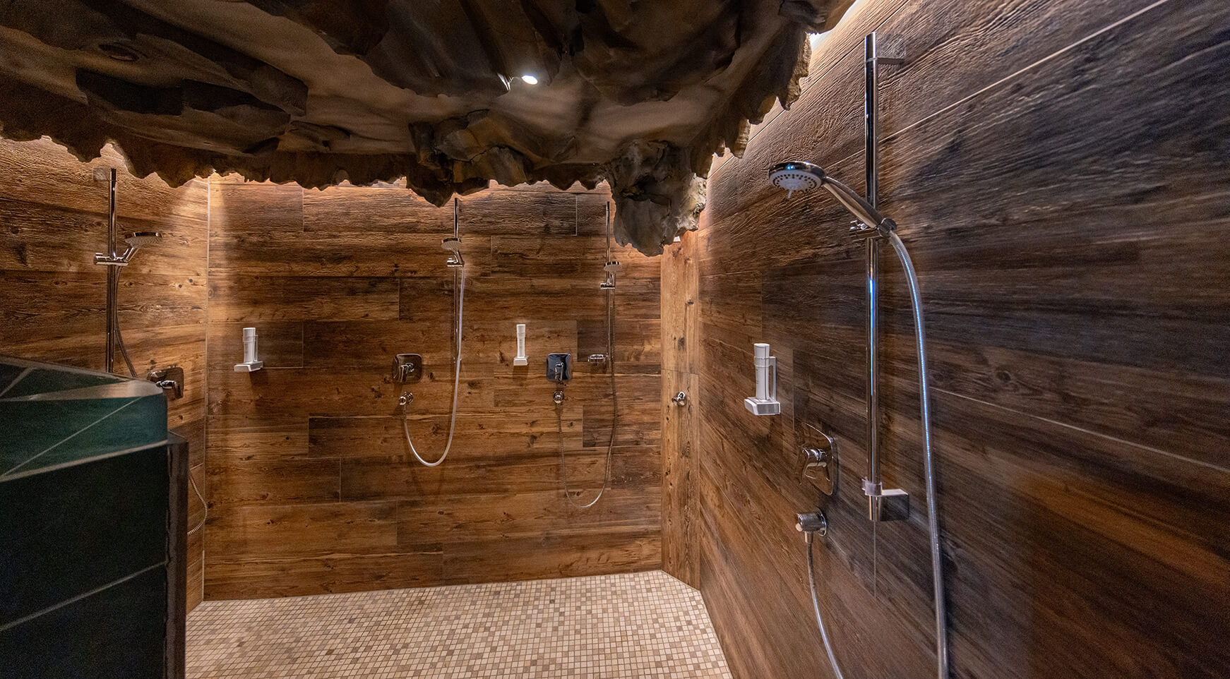 Mehrere Duschen, Holzwände, Mosaikboden, Felsendecke.