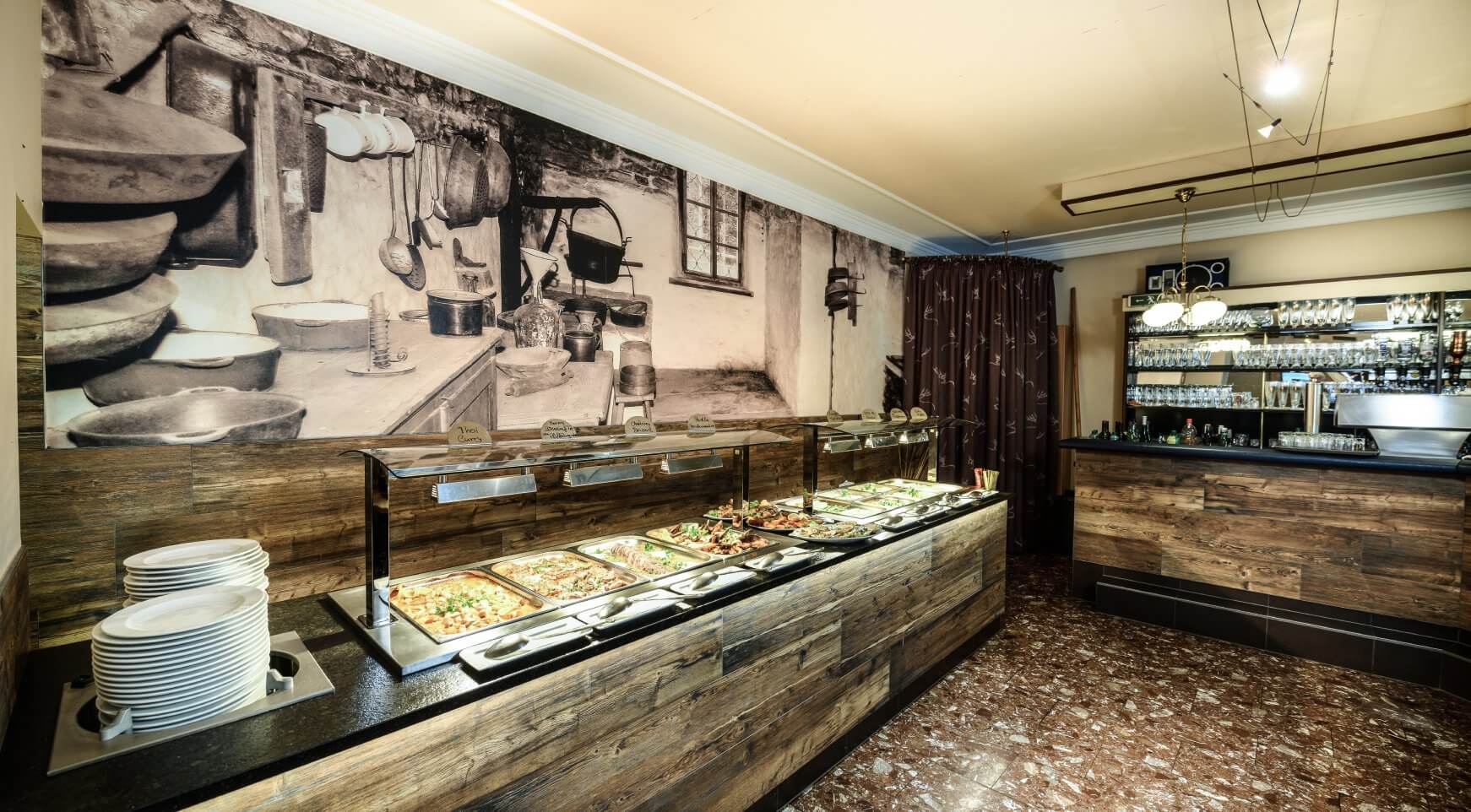 Buntes Buffet mit warmen Speisen, Bar und Küchen-Wandbild.